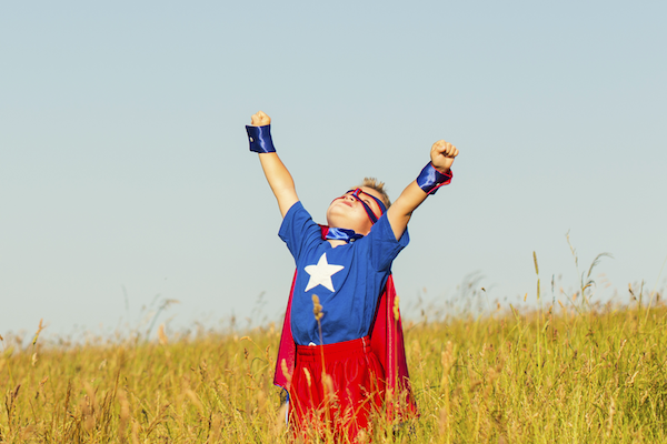 Superhero girl doing powerful pose against blue sky background